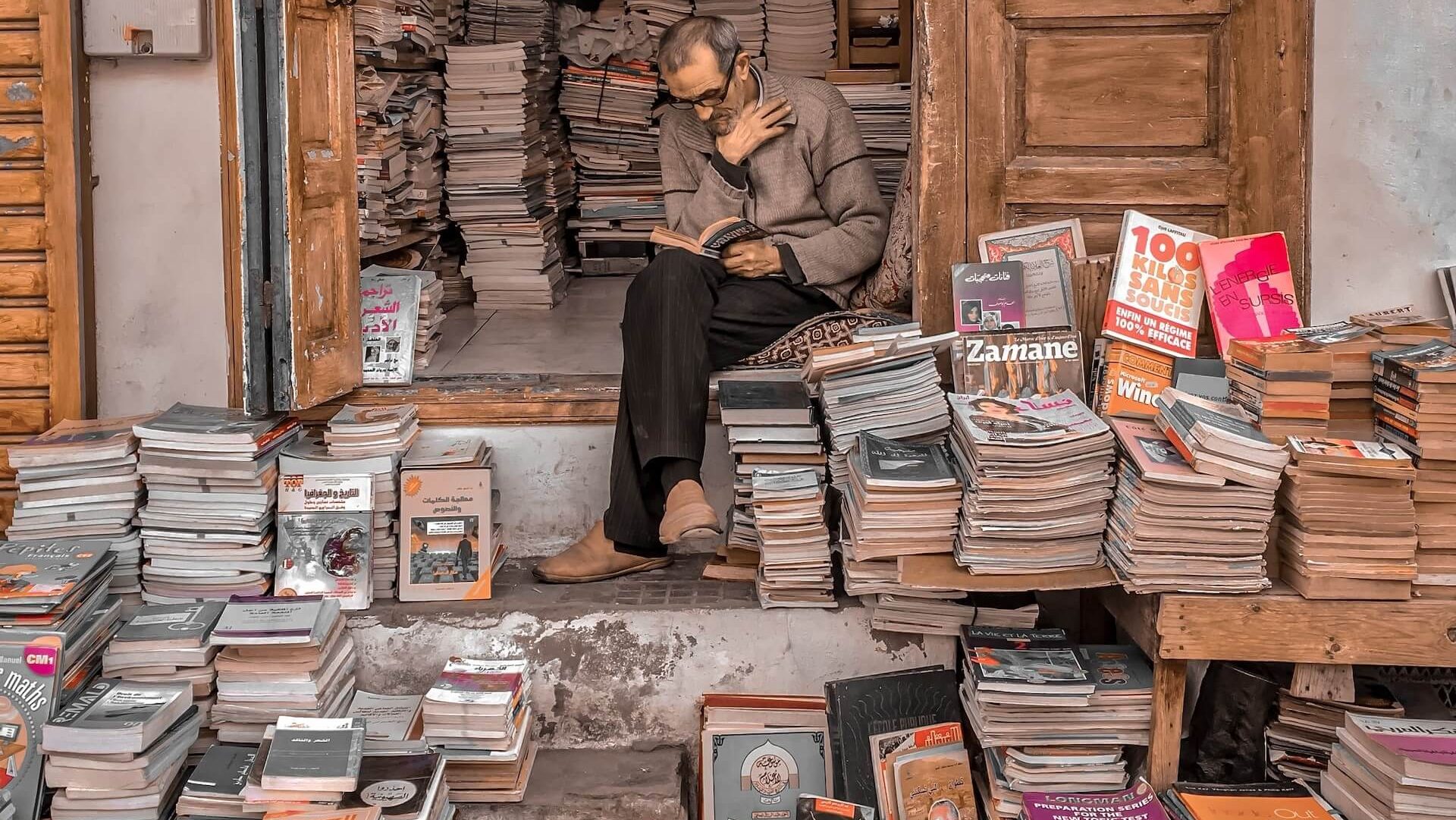 Uomo seduto sulle scale, immerso in un libro circondato da una vasta collezione di libri